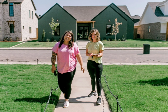 Two smiling women walk towards a modern green house